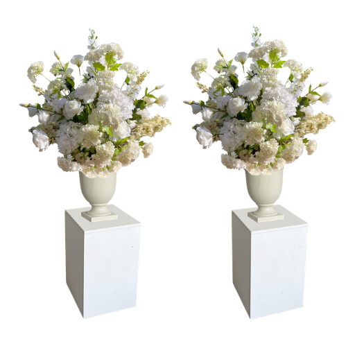 Two matching artificial flower arrangements in white urn-shaped vases, displayed on white rectangular pedestals against a plain white background. Saratoga Lake George New York Floral Rentals